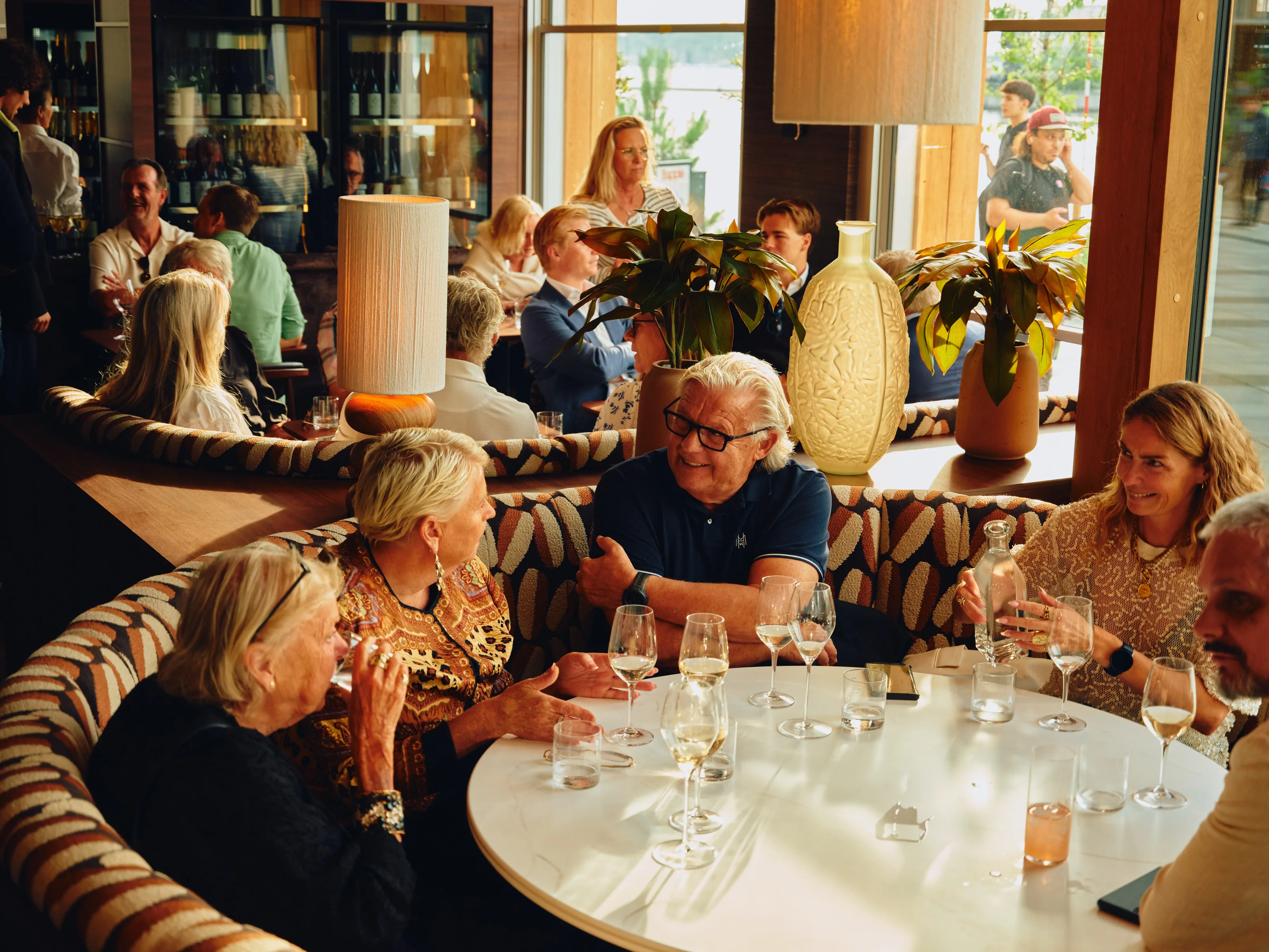 Gjester samlet rundt et restaurantbord med vinglass i varmt lys
