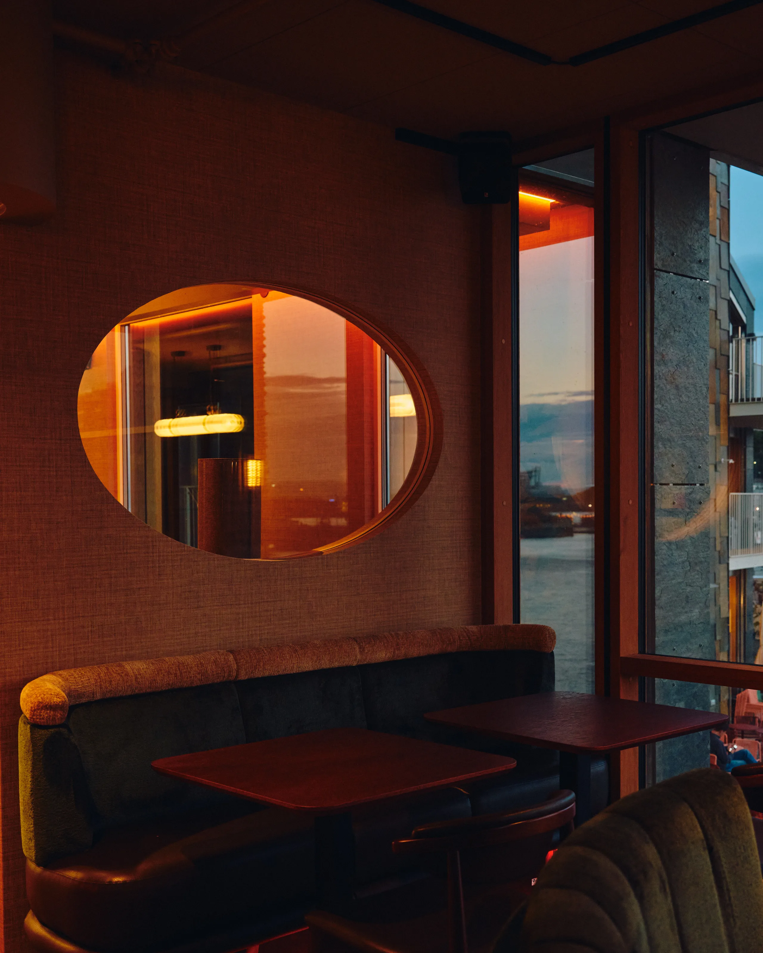 Varmt opplyst restaurantinteriør med ovalt speil og utsikt mot sjøen